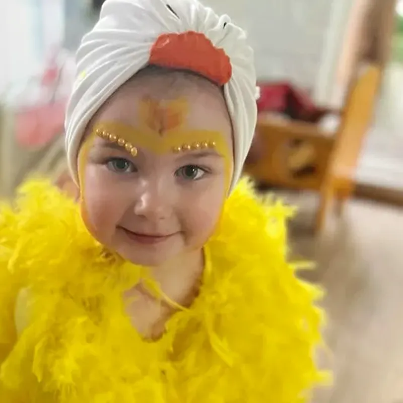Imagination takes flight at Bluebird! Through dress-up, role play, and creative activities, children build confidence, express themselves, and enjoy learning through fun-filled experiences. A young child dressed in a bright yellow bird costume sits on a classroom floor during a dress-up activity, smiling at the camera while other children participate in the background.
