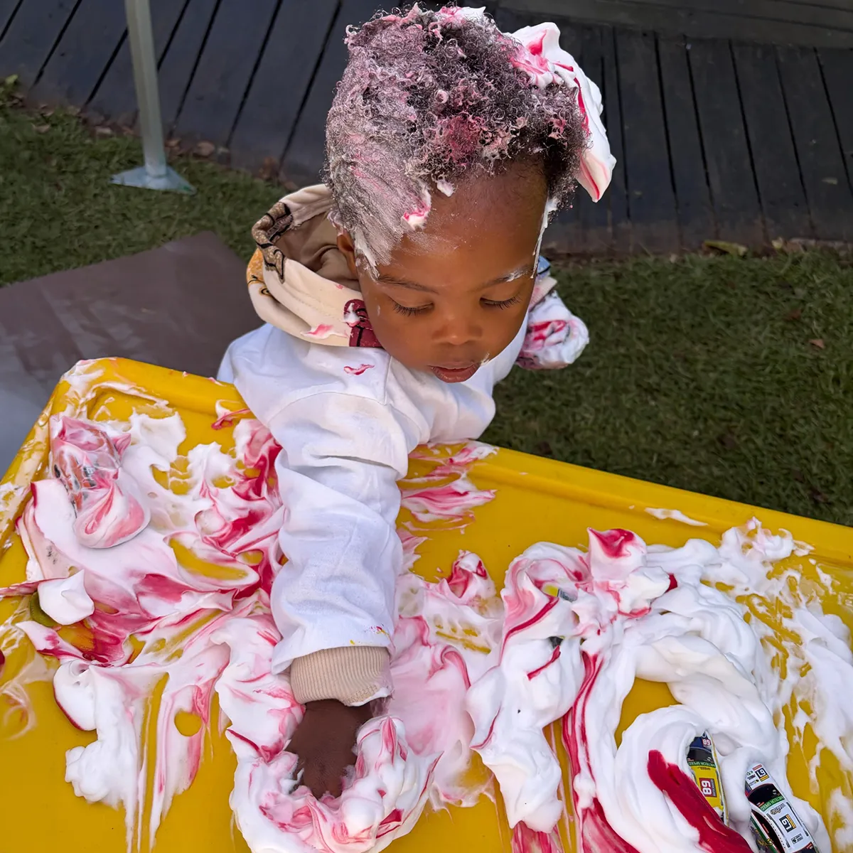 Young child enjoying outdoor sensory play with colourful shaving cream at Bluebird Pre-Primary.