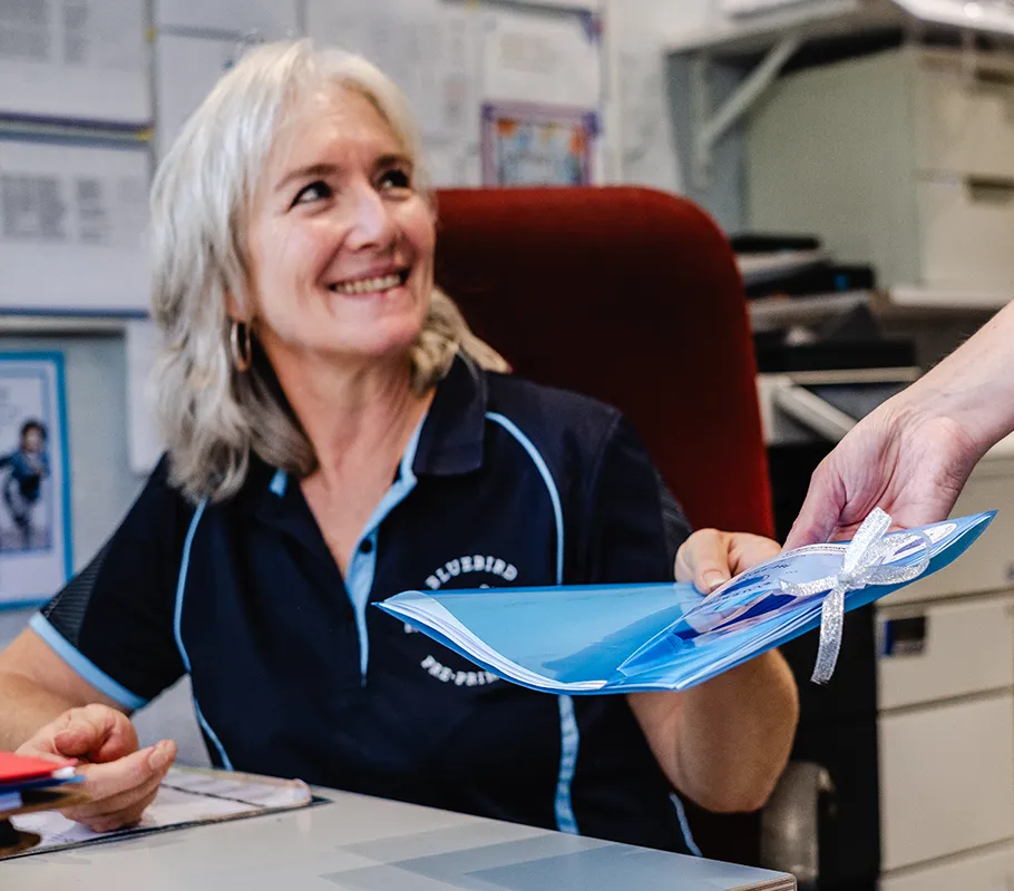 A safe space to play, explore and grow. Bluebird Pre-Primary staff member smiling as she receives completed forms at the school office.
