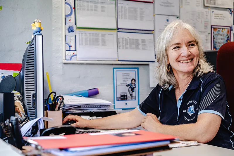 Smiling Bluebird Pre-Primary staff member seated at her desk in the school office.